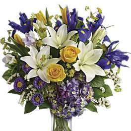 Bouquet of white lilies, yellow roses, and purple flowers in a glass vase