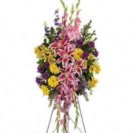 Standing floral spray with pink lilies, yellow daisies, and purple flowers on an easel
