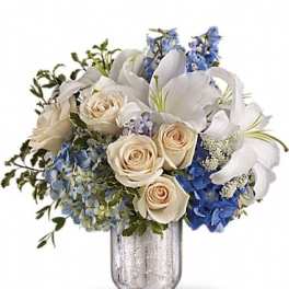 White lilies, cream roses, and blue flowers in a glass vase