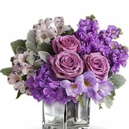 Purple roses and mixed lavender flowers in a clear glass vase