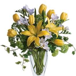 Yellow tulips and pale lavender flowers in a clear glass vase