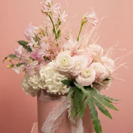 Pastel bouquet of white and blush flowers in a pink hatbox