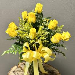 Yellow roses arranged in a clear vase with a yellow ribbon bow