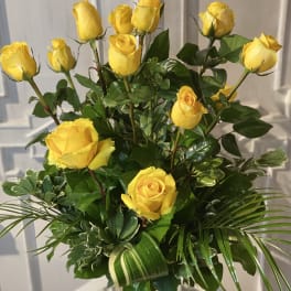 Yellow roses arranged in a clear glass vase with glossy greenery