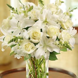 White lilies and roses in a clear glass vase on a wooden table