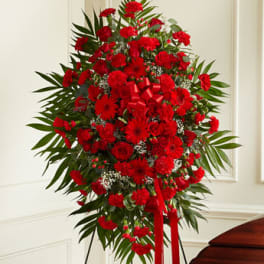 Tall standing spray of red roses, carnations, and gerbera daisies with red ribbon on an easel