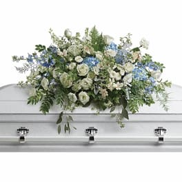 White and blue funeral casket spray with roses and mixed flowers on a white casket