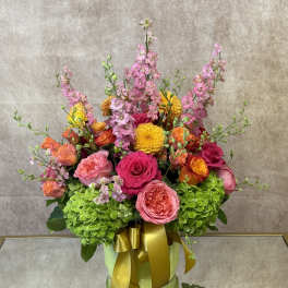 Colorful bouquet of pink, orange, and yellow flowers in a green box with a gold ribbon