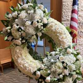 Large white floral wreath on an easel with roses and lilies