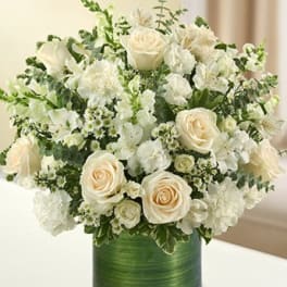 Round arrangement of white and cream flowers in a green-wrapped glass cylinder vase