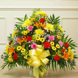 Triangular mixed arrangement of yellow daisies, orange lilies, and red and pink carnations with a yellow bow