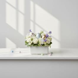 White floral arrangement with pastel Easter eggs in a rectangular vase