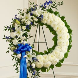 Standing wreath of white flowers with blue accents and a blue ribbon on a metal easel