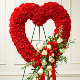 Standing red heart-shaped wreath of carnations with white roses and red ribbon on an easel
