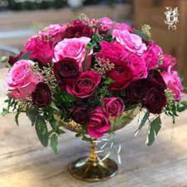 Low centerpiece of hot pink and dark red roses arranged in a gold pedestal bowl