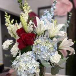 Bouquet of red roses, white lilies, and blue hydrangeas in a glass vase