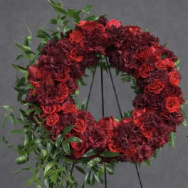 Red floral wreath on a black stand with trailing greenery