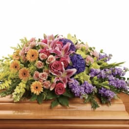 Colorful floral spray on a wooden casket with pink lilies and purple blooms
