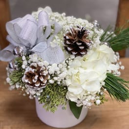 White floral arrangement with pinecones and a silver ribbon in a white container