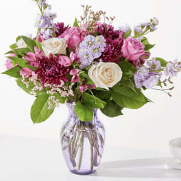Pink, cream, and purple mixed flower arrangement in a lavender glass vase