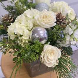 White roses and hydrangeas arranged with pinecones and silver ornaments in a vase