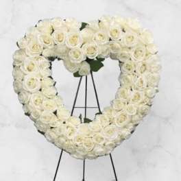 Heart-shaped white rose wreath on a black stand with a white bow