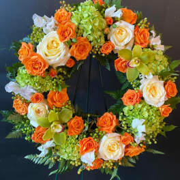 Circular floral wreath with orange and white roses and green orchids on a stand