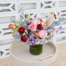 Mixed bouquet of roses, tulips, and blue flowers in a green glass vase