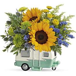 Sunflowers and blue flowers arranged in a small camper-shaped container