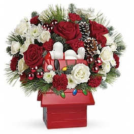 Red and white Christmas flower arrangement in a Snoopy doghouse container with pinecones and ornaments