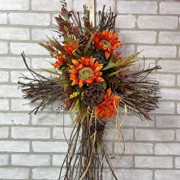 Orange floral cross with branches and pinecones on a brick wall