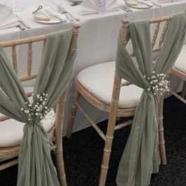 Chiavari chairs with sage drapes and small white floral accents at a set table