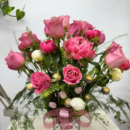 Pink roses and peonies arranged in a glass vase with a pink ribbon