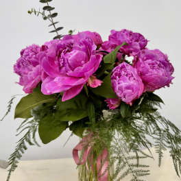 Pink peonies arranged in a clear glass vase with trailing greenery