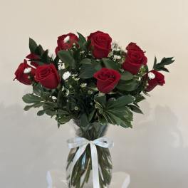 Bouquet of red roses and small white filler flowers in a glass vase with a white ribbon.