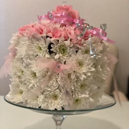 Pink and white flower arrangement on a glass pedestal stand with ribbon bows