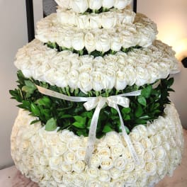 Tiered arrangement of white roses with green foliage and a ribbon