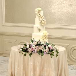 Four-tier white wedding cake with blush flowers and candles on the floor