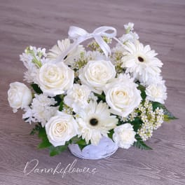 White roses and daisies arranged in a white basket with a ribbon bow