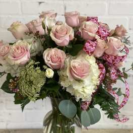 Pink roses and white blooms arranged in a glass vase with heart ribbon