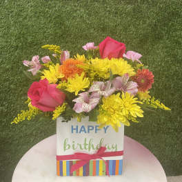Birthday flower arrangement in a striped gift box with pink roses and yellow daisies