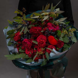 Bouquet of red roses with dark berries and greenery wrapped in blue paper