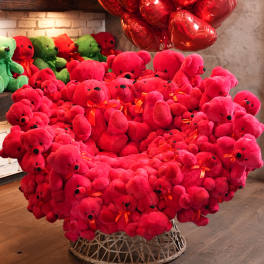 Large heart-shaped display of red teddy bears with red balloons above