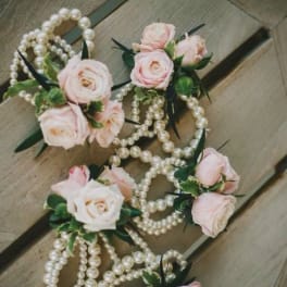 Pink rose corsages with pearl strands on a wooden surface