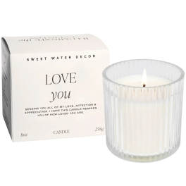 White candle in a ribbed glass holder beside a gift box