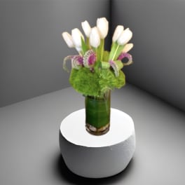White tulips in a green glass vase with purple accent flowers