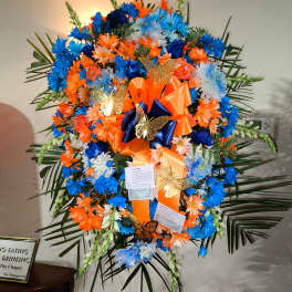 Large standing floral spray in blue, orange, and white with ribbons and butterflies