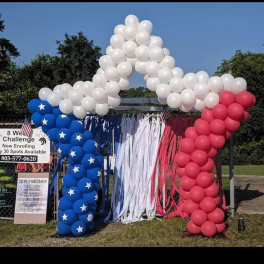 Red, white, and blue balloon arch with hanging streamers outdoors