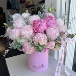 Pink peonies and roses arranged in a pink hat box with ribbon