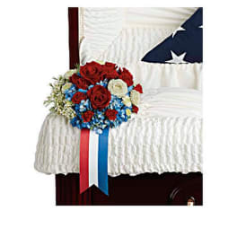 Red, white, and blue floral arrangement on a draped casket with an American flag